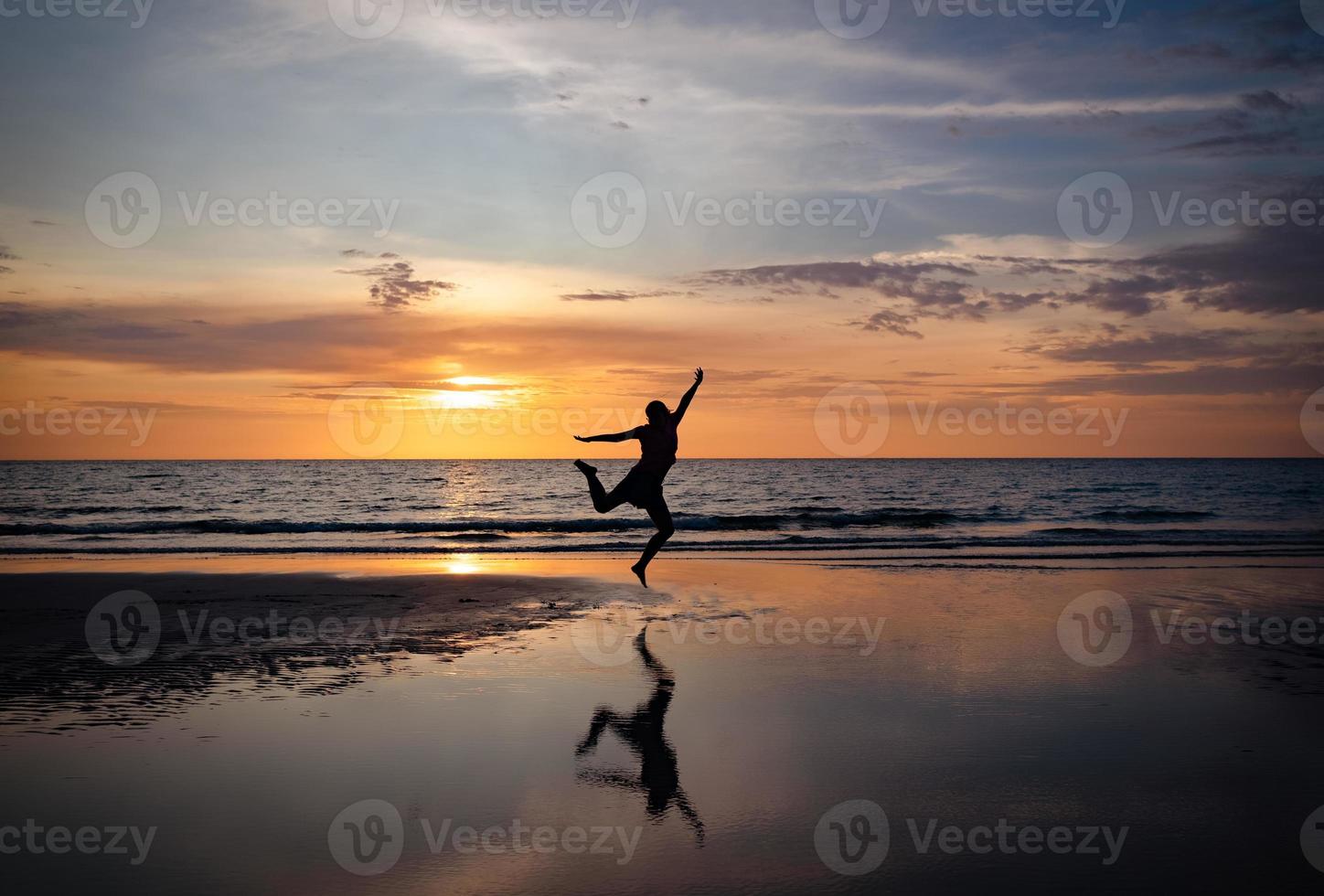 silhouet van een vrouw die op het strand springt bij zonsondergang foto