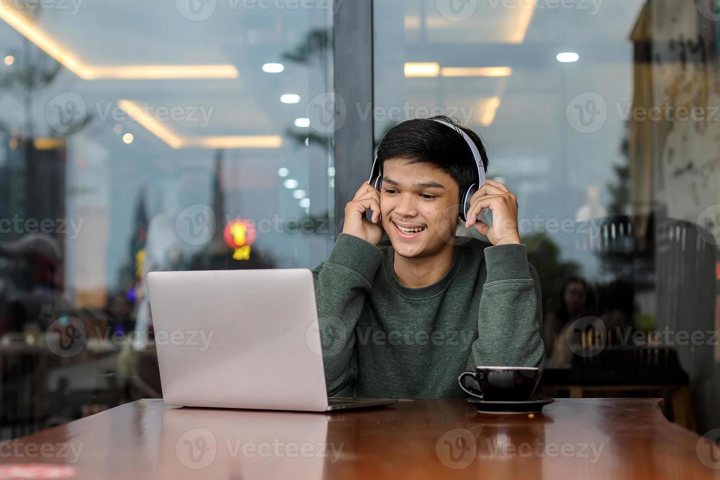 Aziatische mannelijke student die online studeert met een laptop in het café of de coffeeshop foto