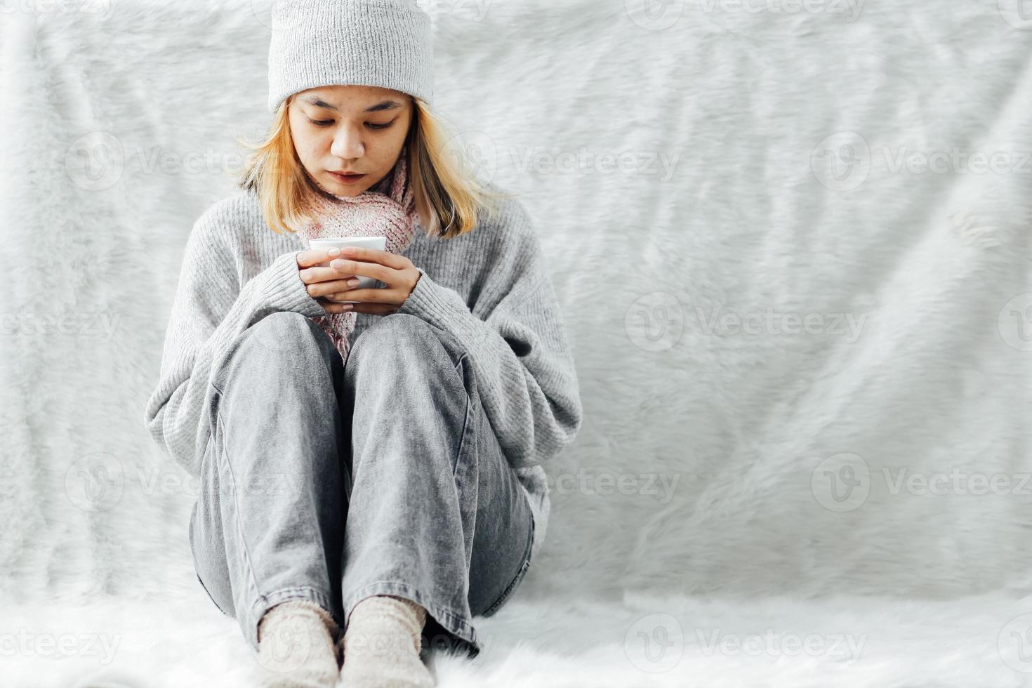 een meisje met winterkleren die in de winter thuis genieten van een kopje warme drank foto