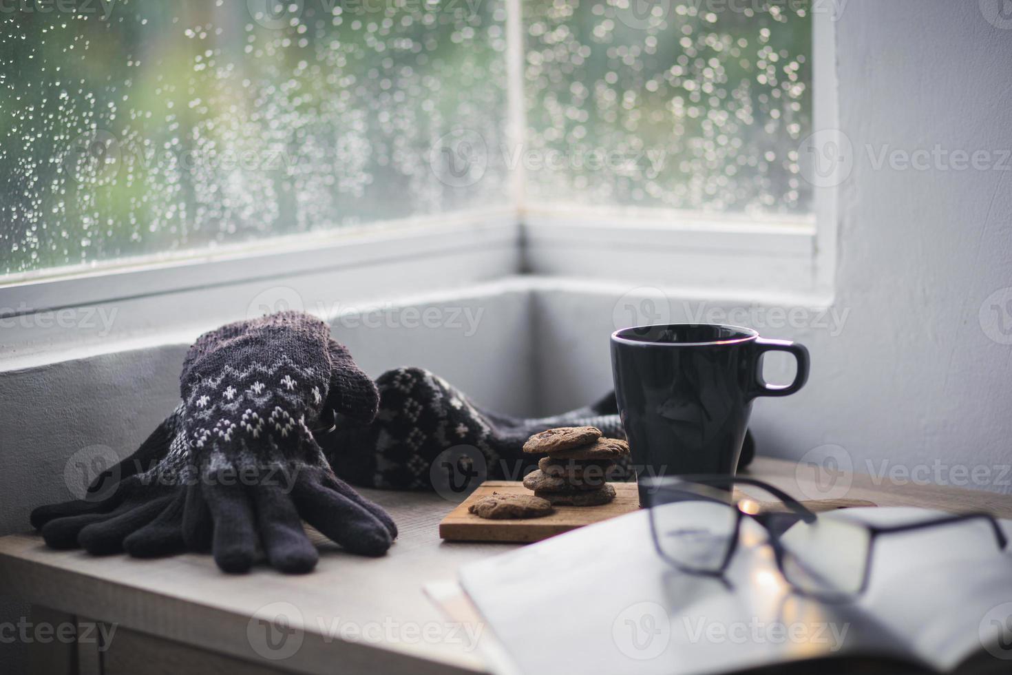 winterhandschoenen en muts met een kopje koffie en koekje op houten tafel voor winterachtergrond foto