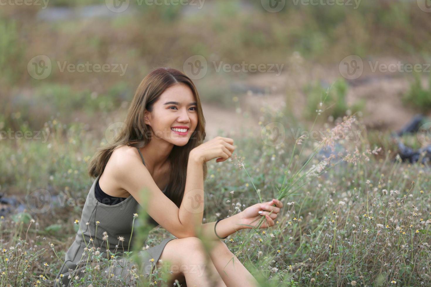 mooie jonge vrouw zittend op het veld in groen gras en paardebloem waait. buitenshuis. geniet van de natuur. gezond glimlachend meisje op de lentegazon. allergievrij concept. vrijheid foto