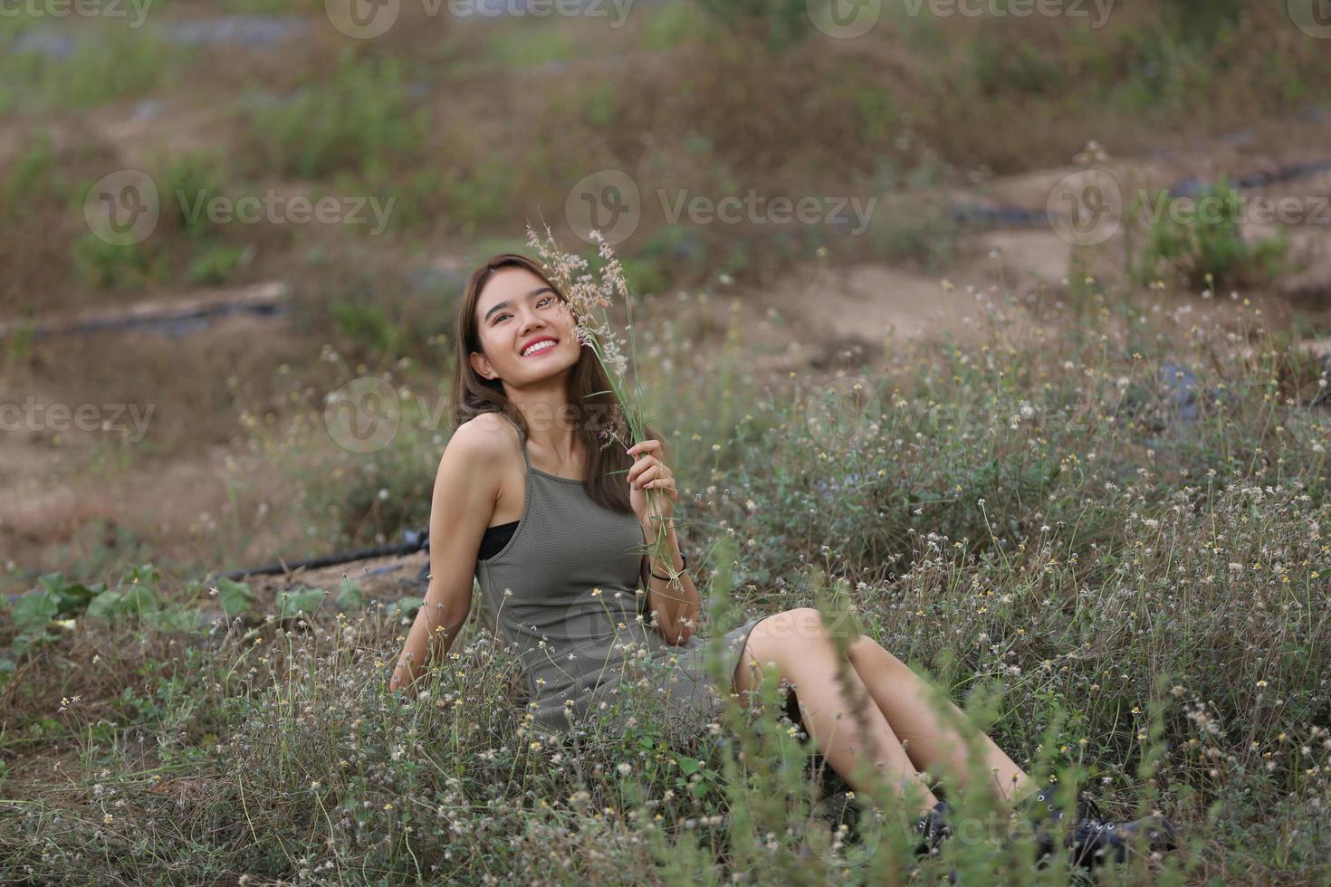 mooie jonge vrouw zittend op het veld in groen gras en paardebloem waait. buitenshuis. geniet van de natuur. gezond glimlachend meisje op de lentegazon. allergievrij concept. vrijheid foto