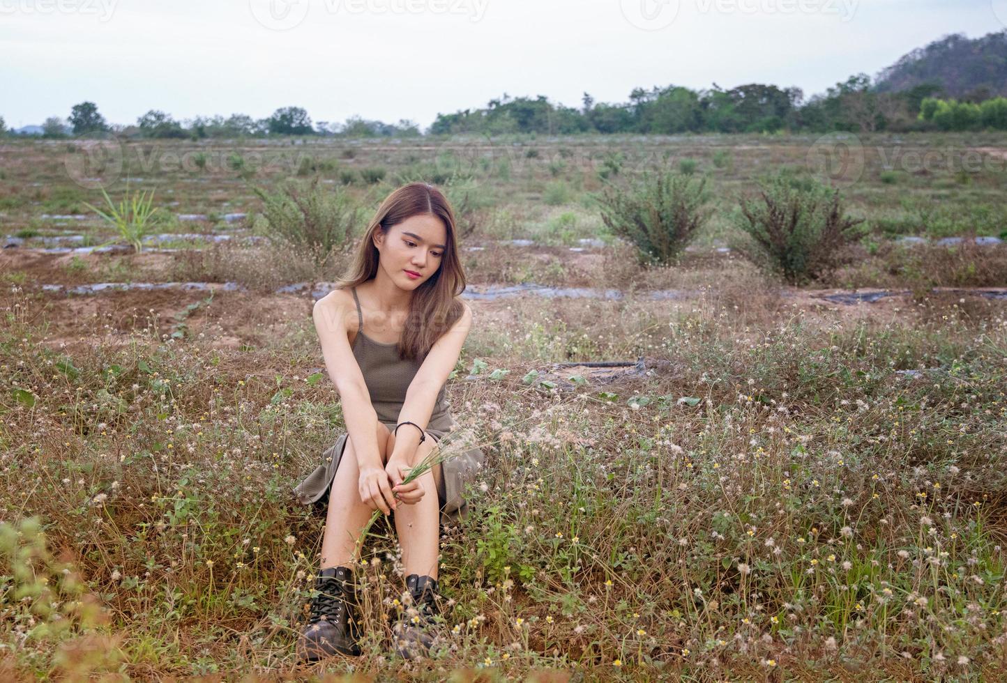 mooie jonge vrouw zittend op het veld in groen gras en paardebloem waait. buitenshuis. geniet van de natuur. gezond glimlachend meisje op de lentegazon. allergievrij concept. vrijheid foto