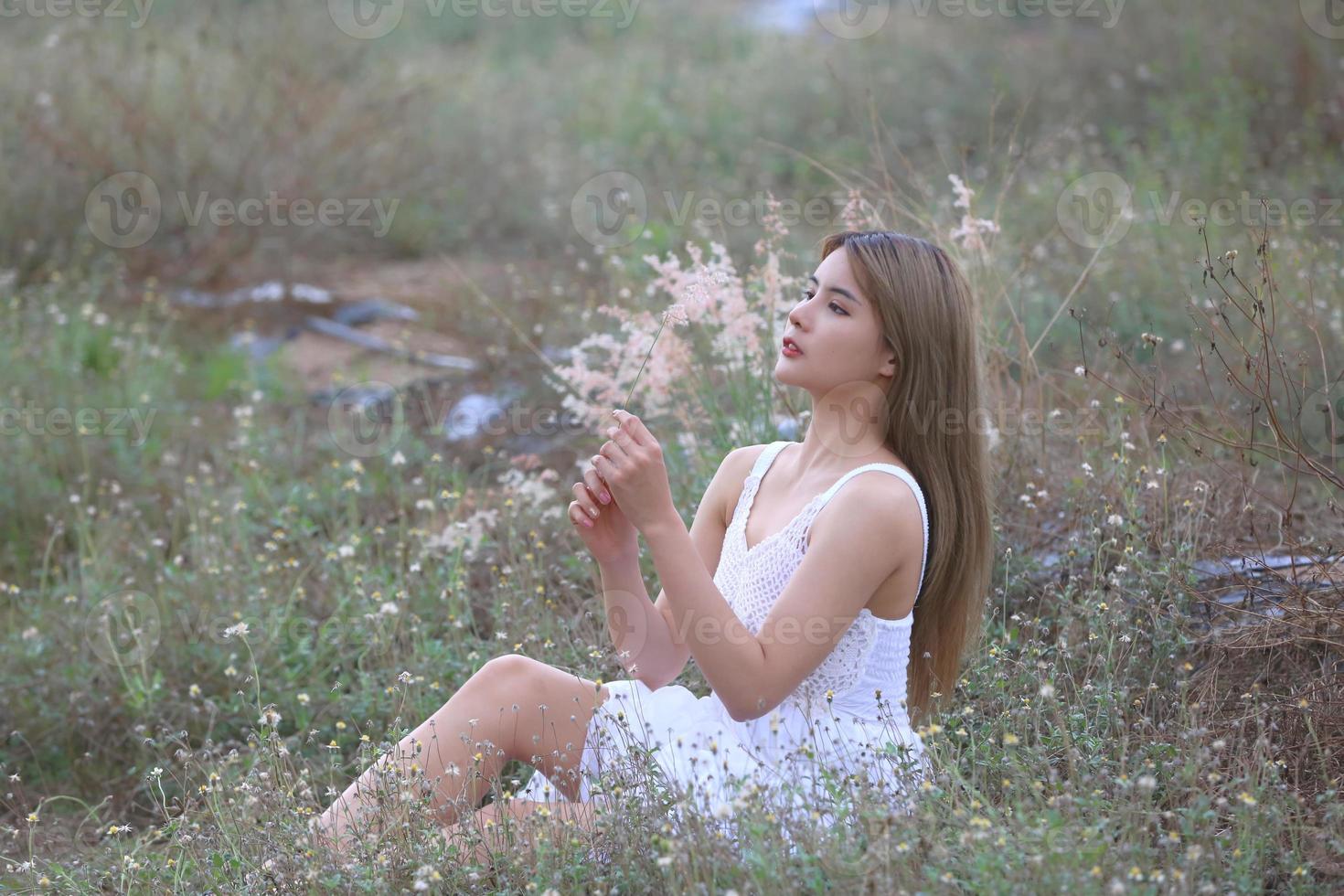 mooie jonge vrouw zittend op het veld in groen gras en paardebloem waait. buitenshuis. geniet van de natuur. gezond glimlachend meisje op de lentegazon. allergievrij concept. vrijheid foto