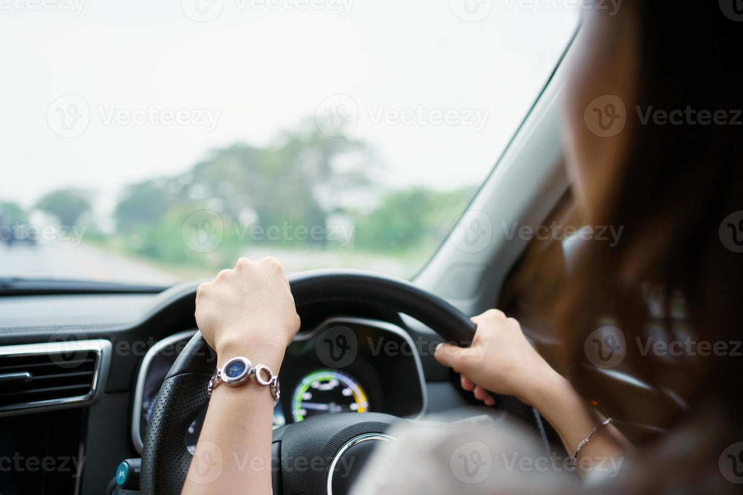 onherkenbare vrouwelijke bestuurder met linkerhandgrepen op het stuur tijdens het rijden op de weg, vrouw rijdt in een moderne elektrische auto ev in prachtig zonlicht op de weg. veiligheid rijden concept. foto