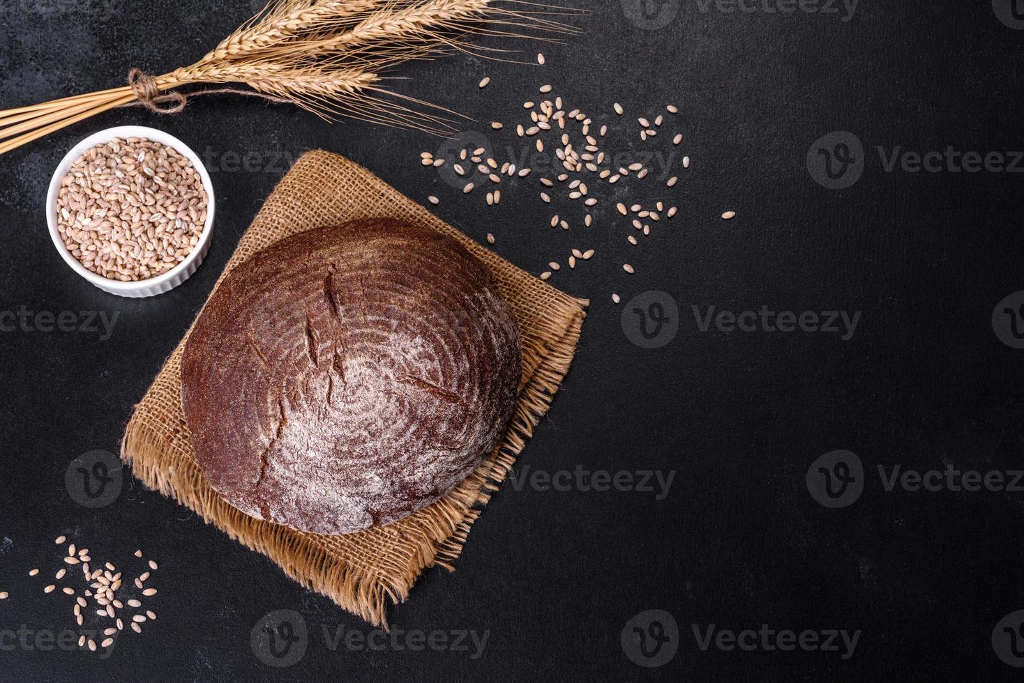 vers gebakken zelfgemaakt bruin brood op een zwarte betonnen ondergrond met tarwekorrels foto