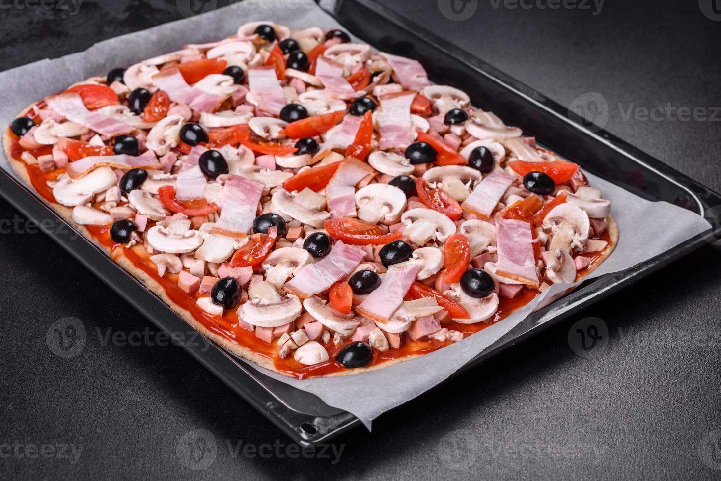 rauwe zelfgemaakte pizza en ingrediënten op zwarte betonnen tafel, bovenaanzicht foto