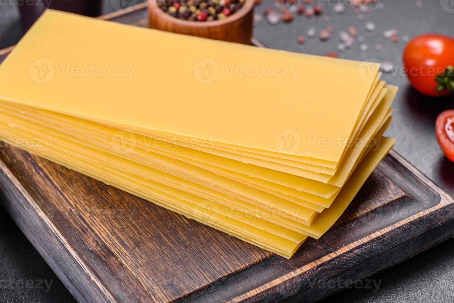 stapel lasagnevellen op een donkere betonnen ondergrond. ingrediënten voor lasagne foto