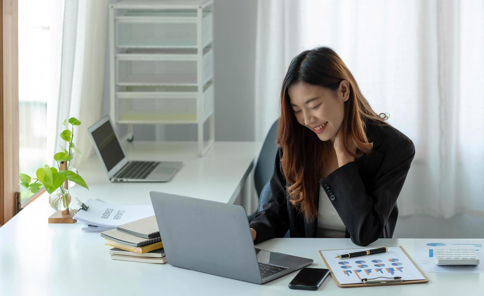 gelukkige jonge Aziatische zakenvrouw zittend op haar werkplek op kantoor. jonge vrouw die werkt op laptop op kantoor. foto