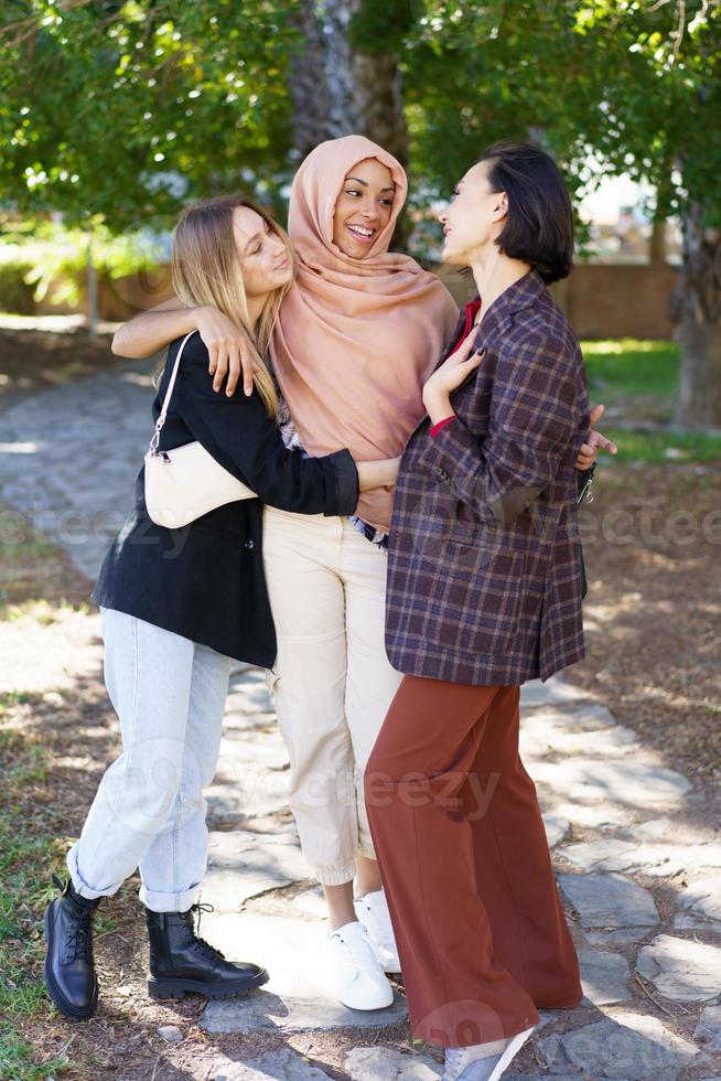 opgetogen jonge diverse vrouwen die omhelzen en glimlachen in het park foto