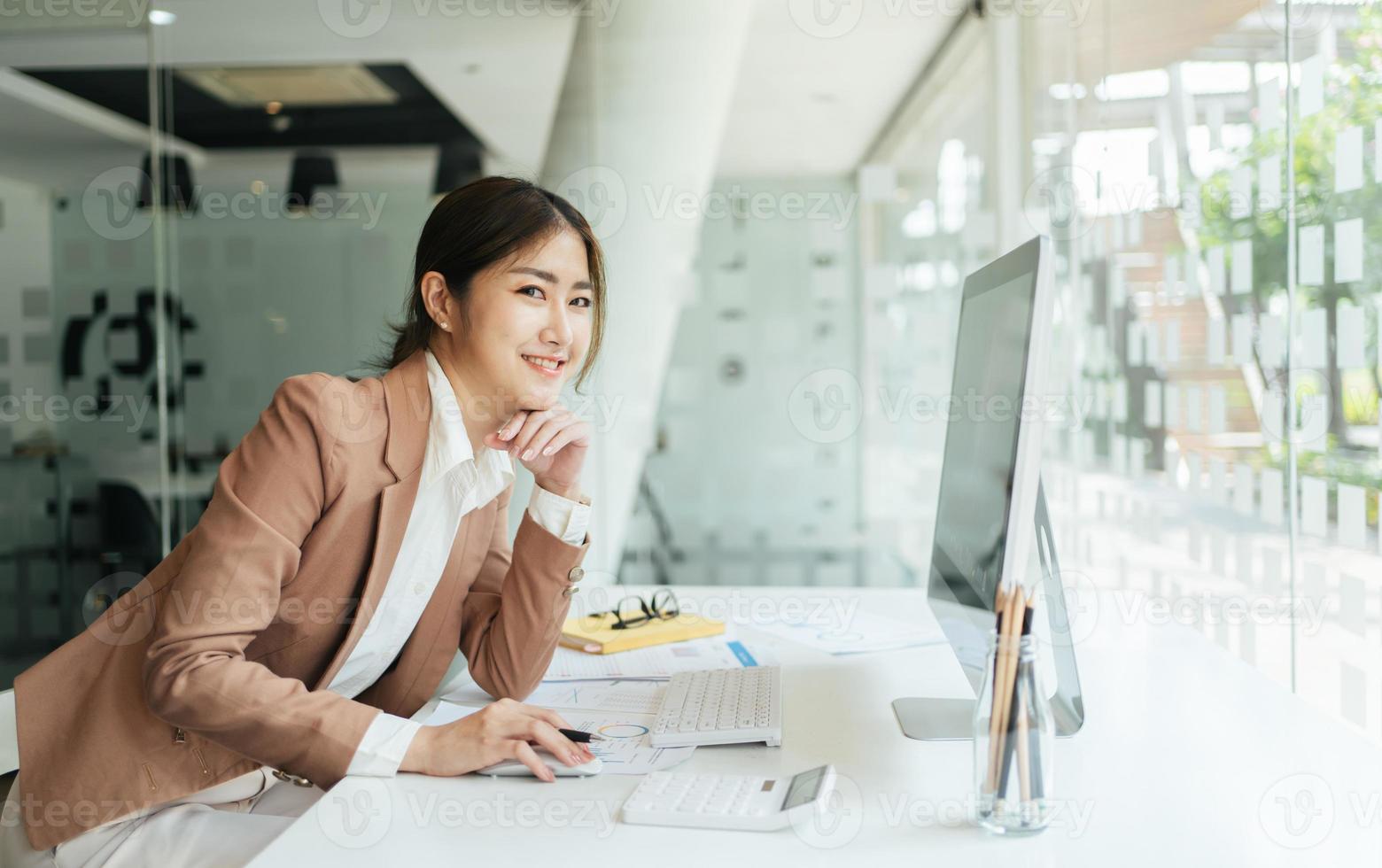 gelukkige aantrekkelijke aziatische zakenvrouw die werkt met een laptop en een financieel document op kantoor, succesvolle actie, bedrijfsconcept. foto