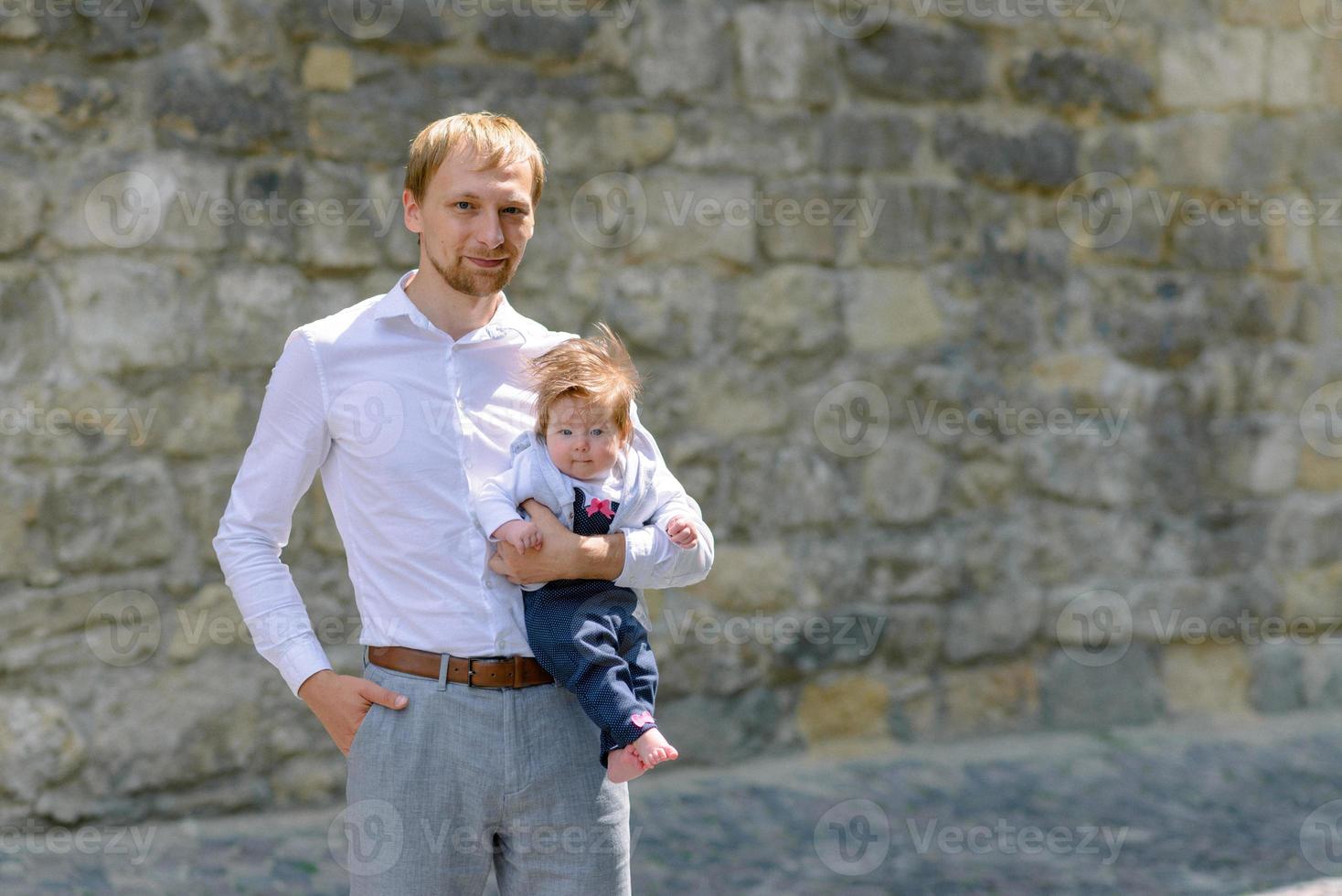 portret van een jonge vader die een huilend babymeisje vasthoudt over een witte bakstenen muur foto