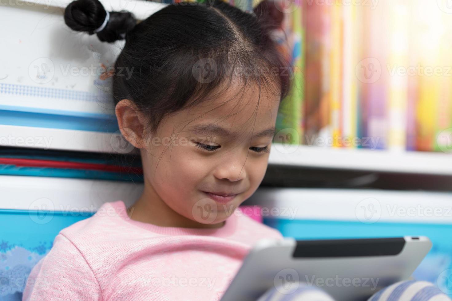 gesloten aziatisch thais meisje kind kind zit boek zelf grappig om tablet te lezen foto