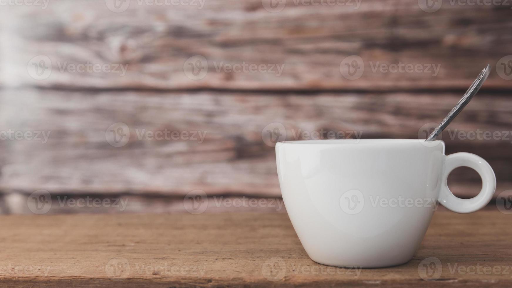 een witte koffiekop met een lepel in de beker wordt op een houten plaat en op een houten ondergrond geplaatst. foto