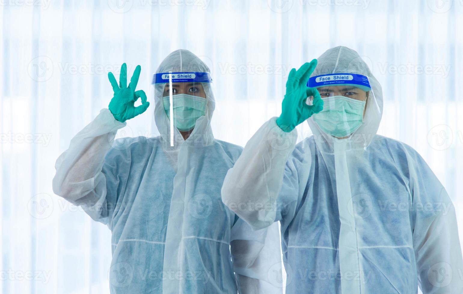 twee medische staf met pbm-pak en gezichtsmasker staande en hand omhoog om te vechten naast ouder wordende vrouwelijke patiënt besmet met corona visrus of covid-19 slaapkamer in quarantainekamer in het ziekenhuis. foto