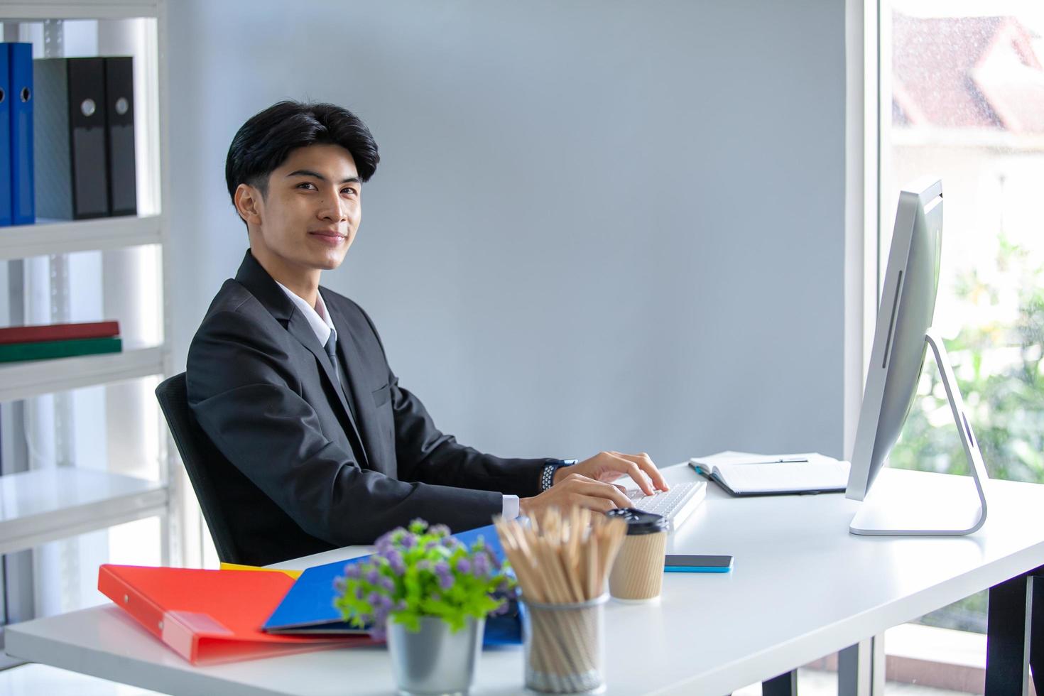 portret van Aziatische knappe man aan het werk op kantoor, met behulp van computer op tafel. foto