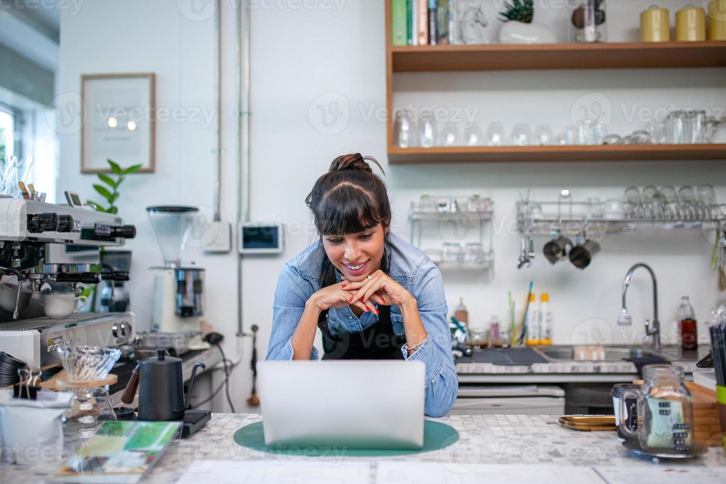gelukkige vrouw barista met behulp van laptop voor bestelling van klant in coffeeshop. foto