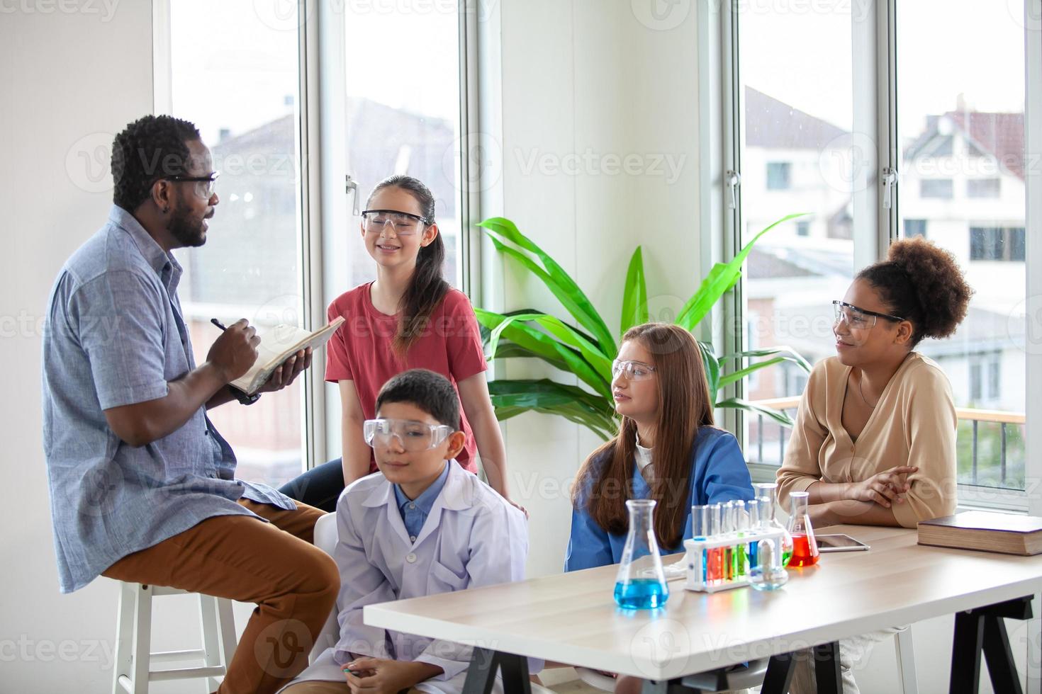 studenten mengen chemicaliën in bekers. enthousiaste leraar legt scheikunde uit aan kinderen, leraar die studenten lesgeeft in de wetenschapsklasse. foto