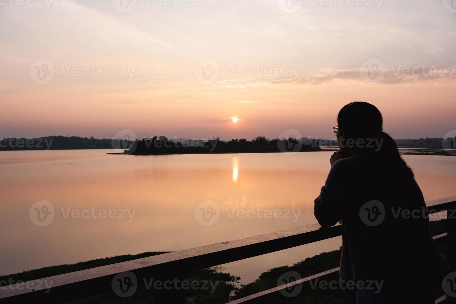 silhouet van de hand van de vrouw die zich in hartvorm vormt rond de zon bij zonsondergang in de buurt van het meer foto