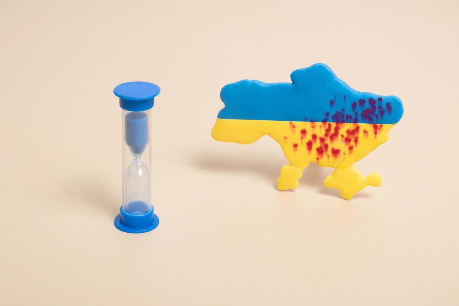 zandloper.en plasticine gele en blauwe kaart van oekraïne met shots en bloed. stop het oorlogsconcept foto