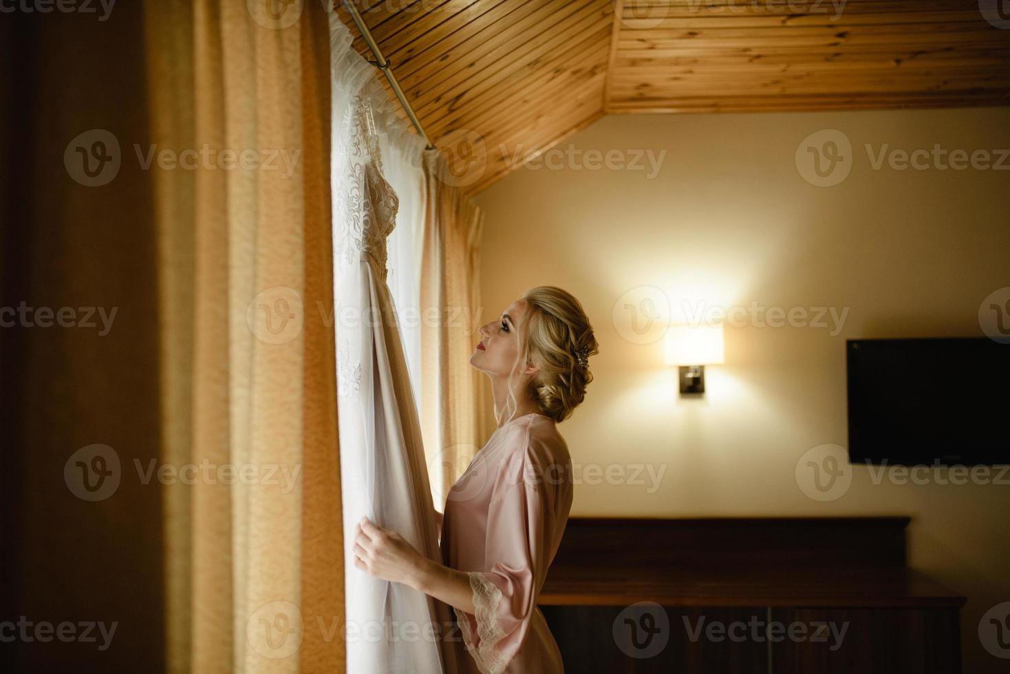 jonge schattige blonde bruid kijken naar haar trouwjurk. foto