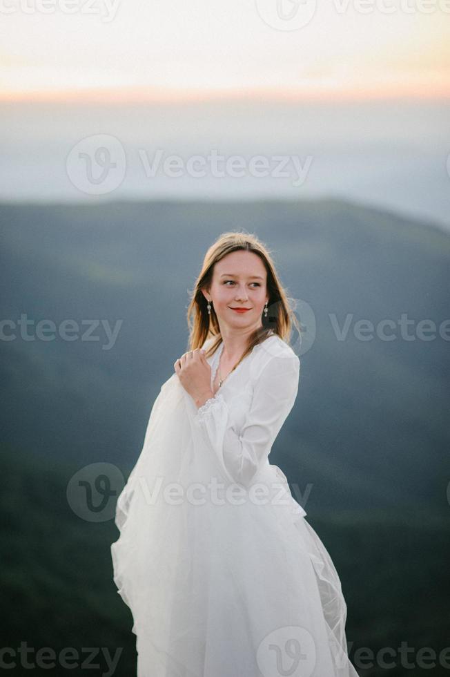 vrouw in trouwjurk rent over het veld naar de bergen foto