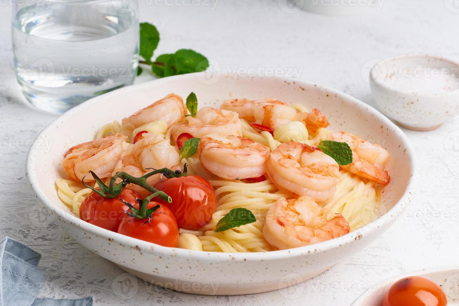 zeevruchten pasta spaghetti met gebakken garnalen, bechamelsaus, muntblad en tomaten op witte tafel foto