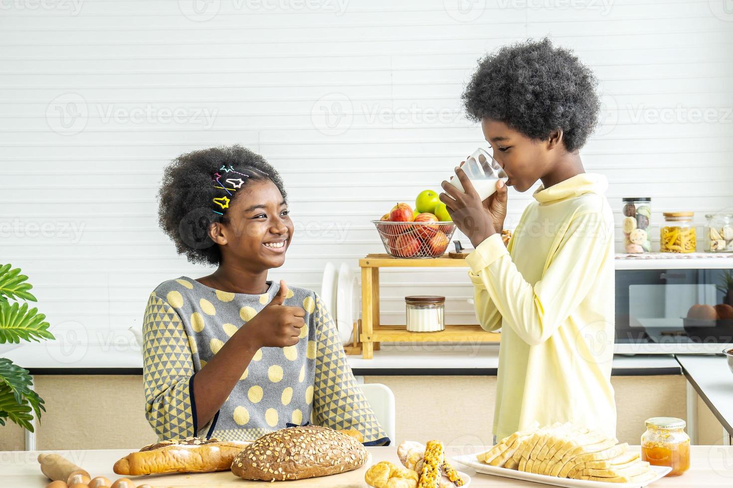 twee schattige schattige broers en zussen Afro-Amerikaanse kinderen die ontbijten met melk in de keuken, portret van gelukkige broer die melk drinkt met zijn zus en duimen omhoog, eten en drinken concept foto