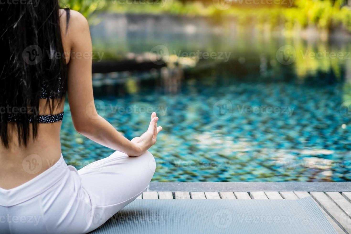vrouw die yoga en meditatie traint in een lotusyoga-positie bij het blauwe zwembad foto