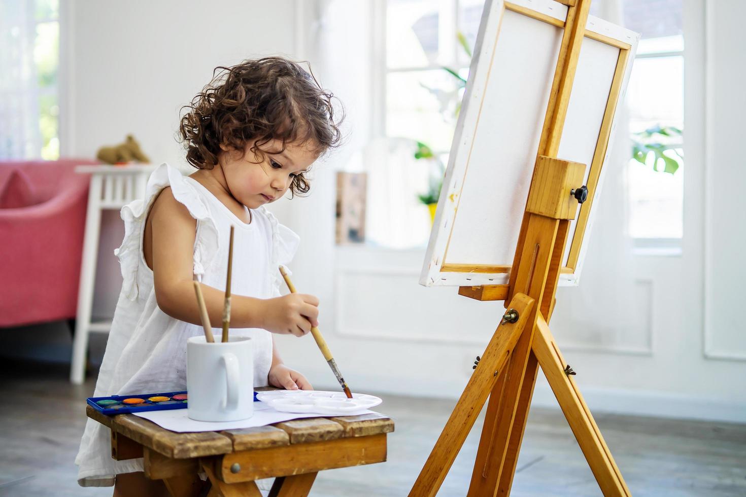 een kleine, schattige meisjeskunstenaar gebruikt een acrylkwast om haar tekeningen op canvas te maken foto
