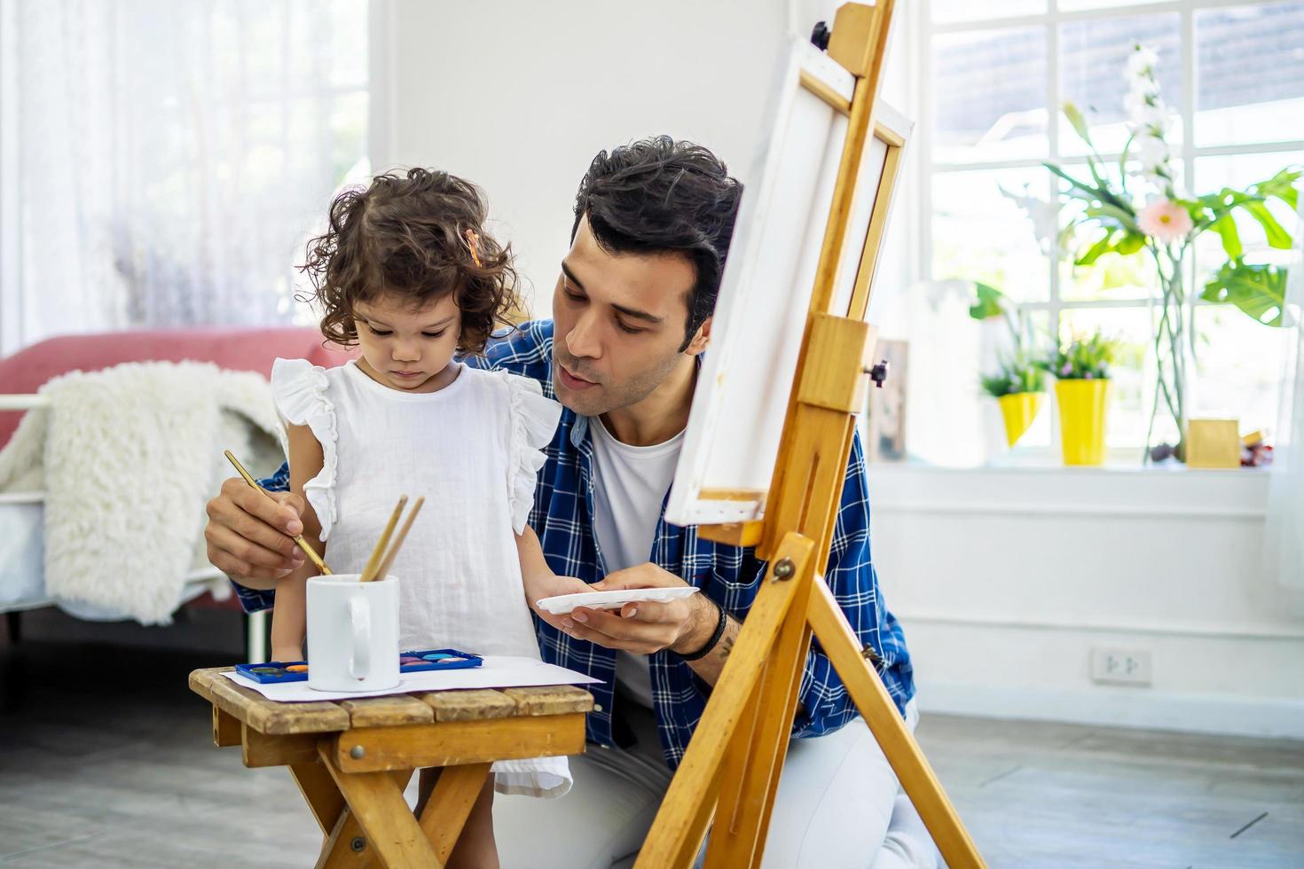 gelukkige familie van vader en kind tekenen foto, met behulp van verschillende verven en penselen. knappe vader en mooi dochtertje tegen oliefoto glimlachen, plezier maken. les van kunst foto