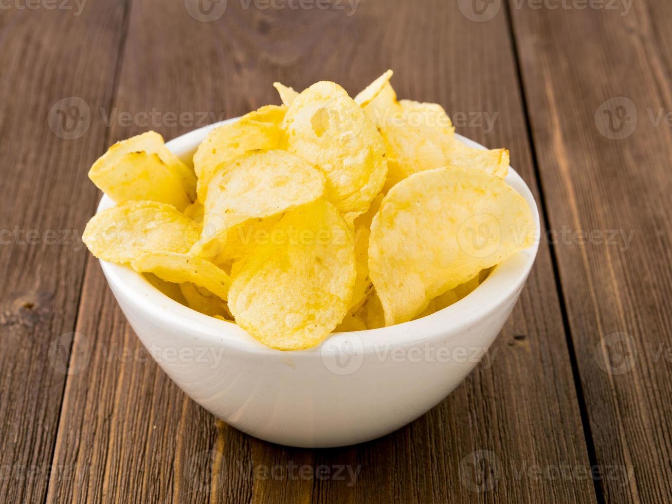 Aardappelchips in witte kom op bruin houten tafel foto