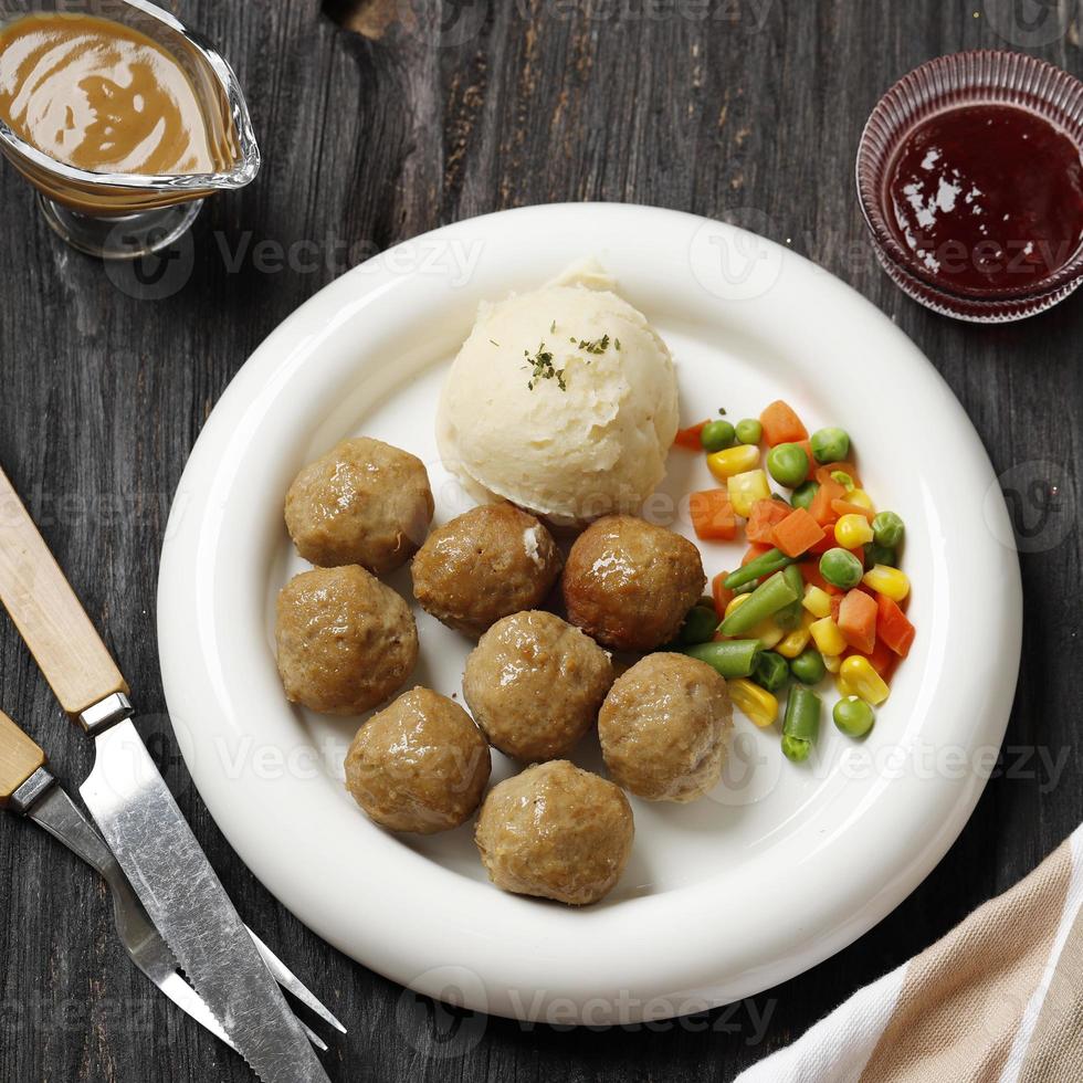 Zweedse gehaktballetjes met romige jus, boterachtige aardappelpuree en bosbessensaus. op wit bord foto
