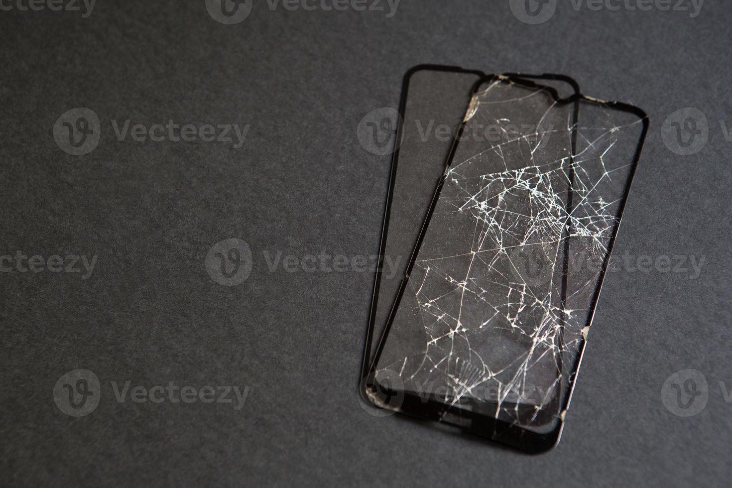 gebroken glas voor uw smartphone. barsten in het beschermglas van het telefoonscherm. beschadigde en nieuwe film op een zwarte achtergrond. kopieer ruimte foto