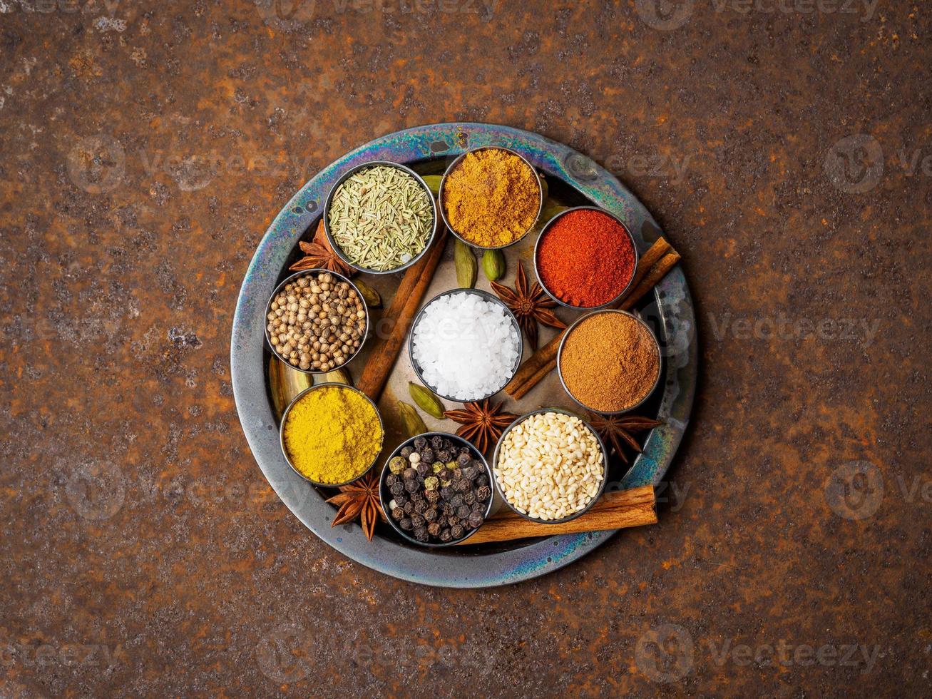 meng kruiden op ronde metalen plaat - korianderzaad, gemalen rode peper, zout, zwarte peper, rozemarijn, kurkuma, curry. bovenaanzicht, close-up, metalen roestige achtergrond. foto