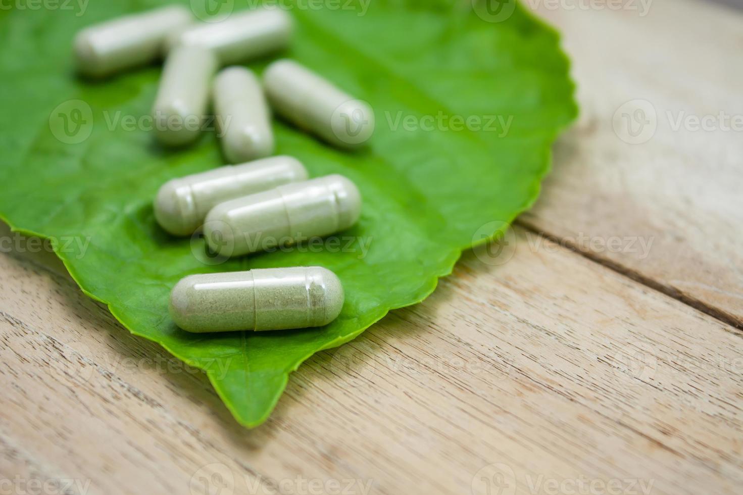 kruidengeneeskundecapsules met groen kruidblad op houten tafel foto