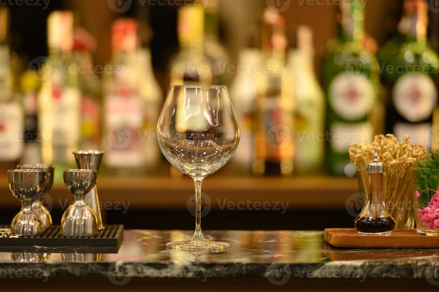 helder glas op zwart marmeren tafelblad en prachtige bokeh-planken met alcoholflessen foto