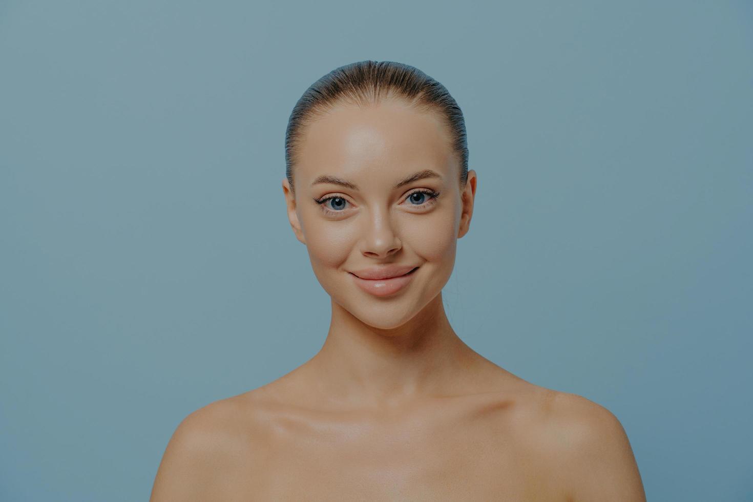 schoonheidsportret van jonge glimlachende schitterende vrouw met perfecte schone gezonde huid die op blauw wordt geïsoleerd foto