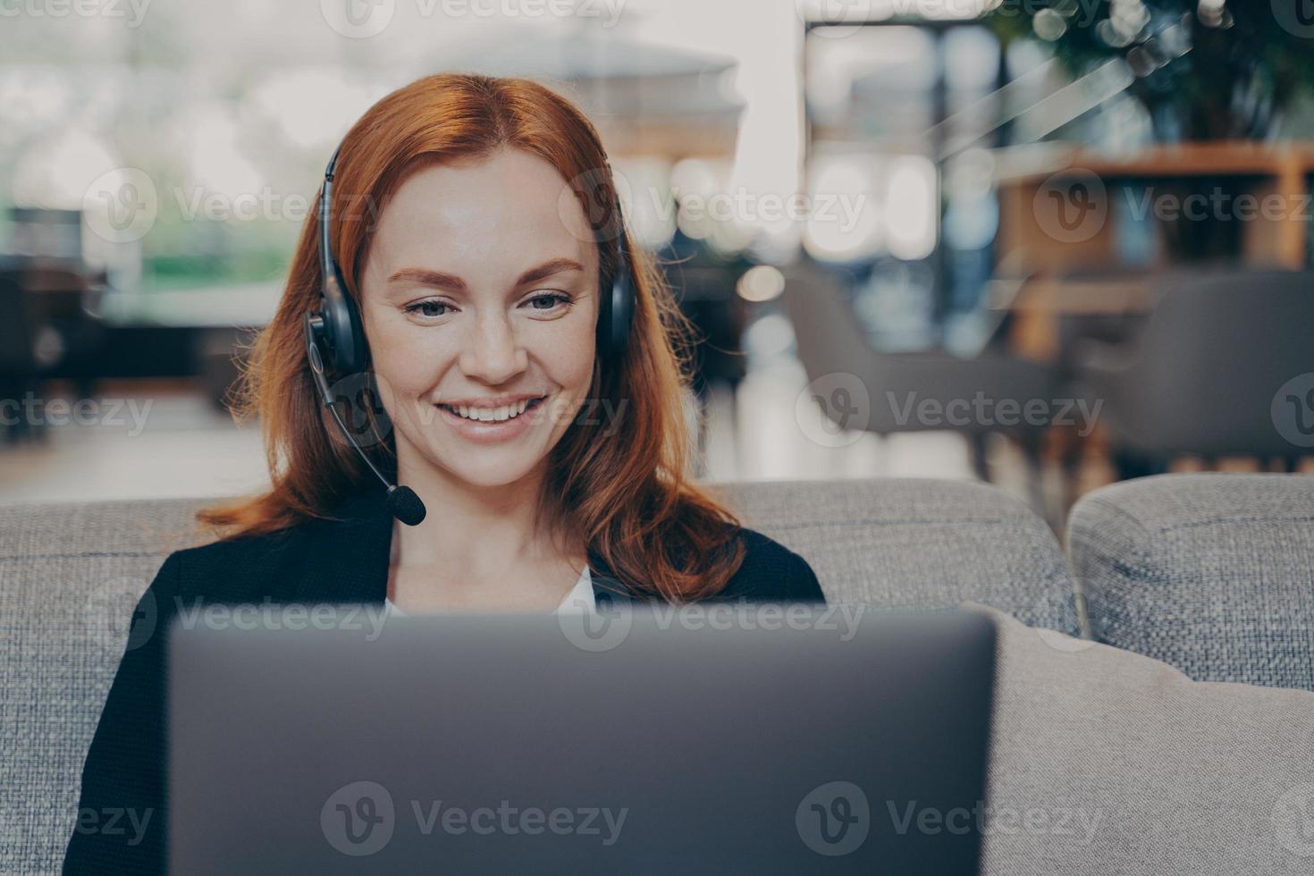 close-up portret van roodharig ondernemersmeisje, op afstand werkend met laptop en koptelefoon-headset foto