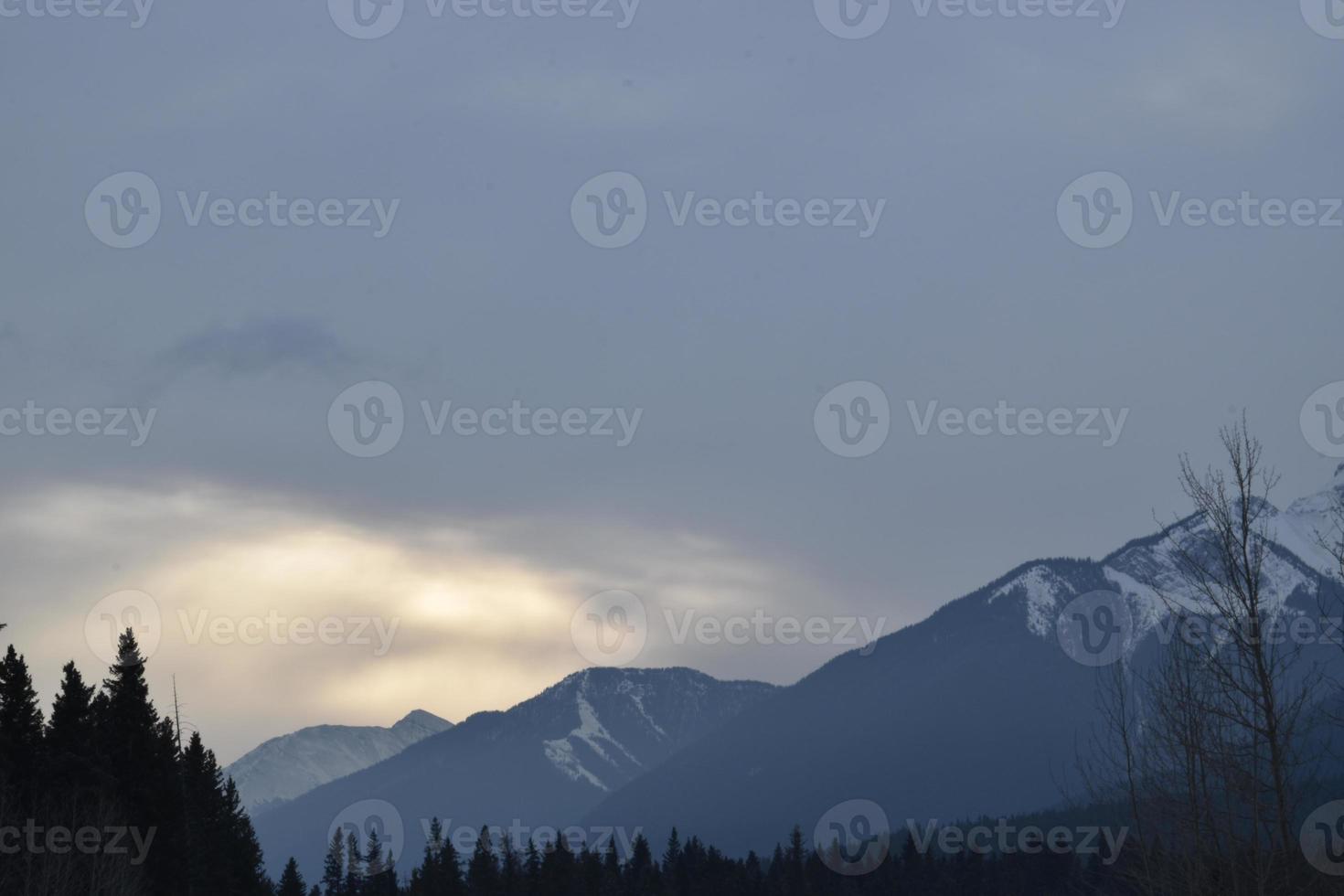 zonlicht wordt geblokkeerd door wolken boven besneeuwde bergtoppen foto