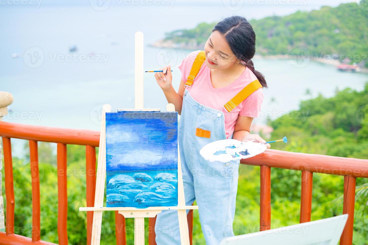 jong meisje met een penseeltekening op canvaspapier, bij een prachtig landschapszicht op koh tao thailand. foto