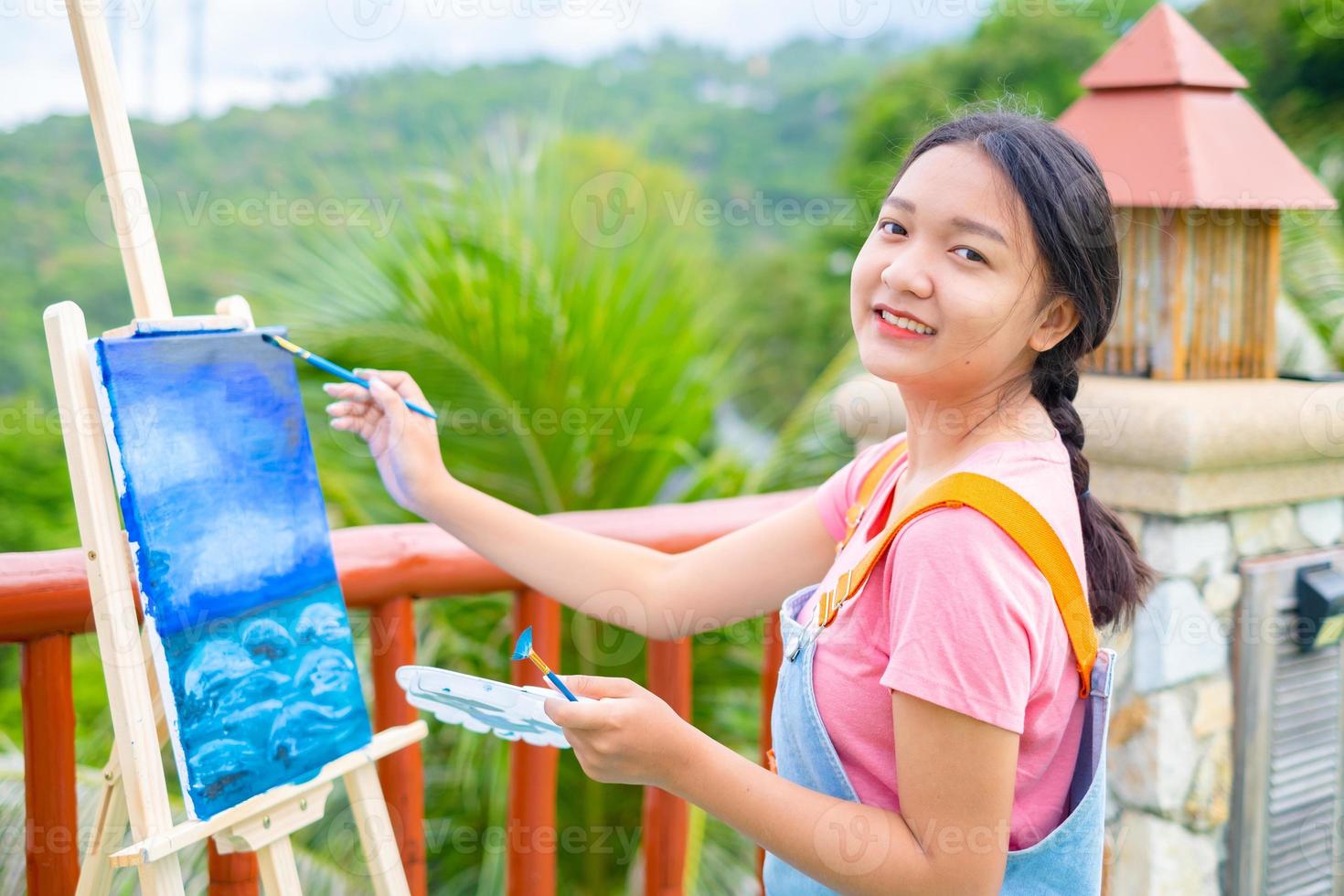 jong meisje met een penseeltekening op canvaspapier, bij een prachtig landschapszicht op koh tao thailand. foto