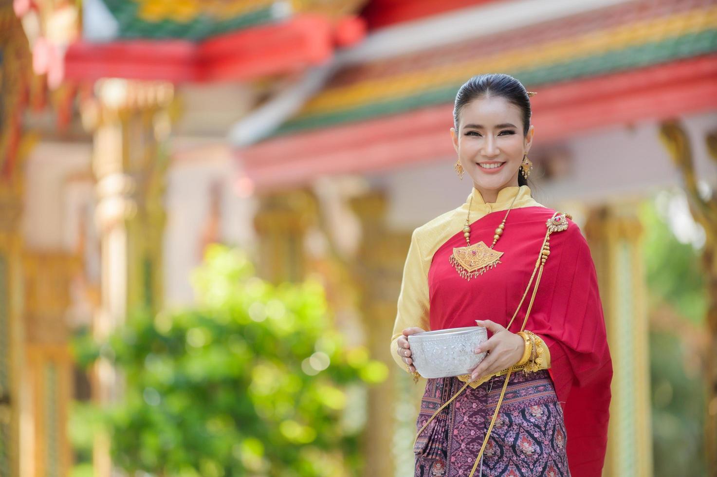 een mooie thaise vrouw in thaise jurk met gouden ornamenten houdt een kopje water vast voor songkran festival of thais nieuwjaar foto