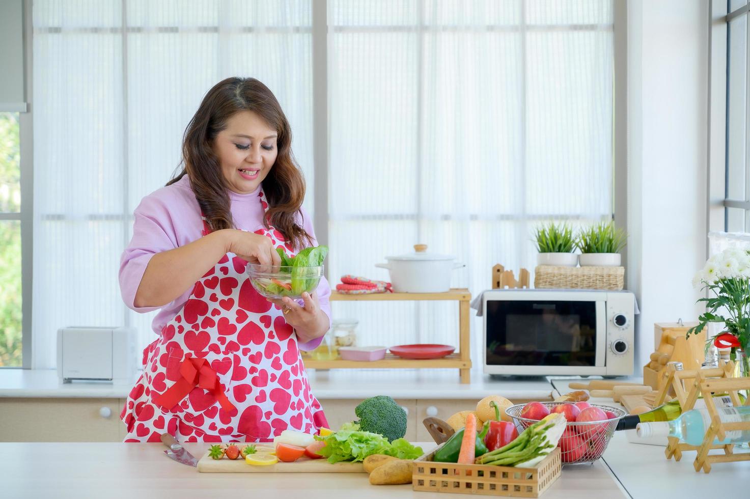 een aziatische vrouw hakt graag een verscheidenheid aan groenten en fruit om een gezonde salade te bereiden voor een op dieet zijnde bejaarde foto