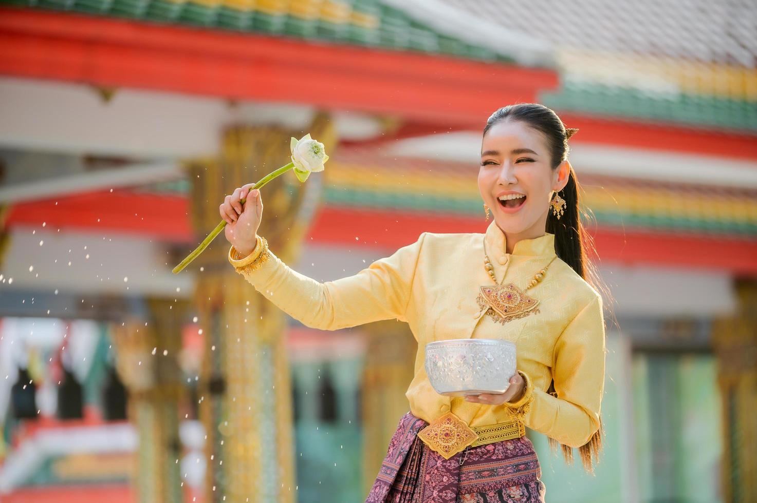 jonge thaise vrouwen in traditionele thaise kleding houden bloemen opspattend water voor de lol op het songkran waterfestival foto