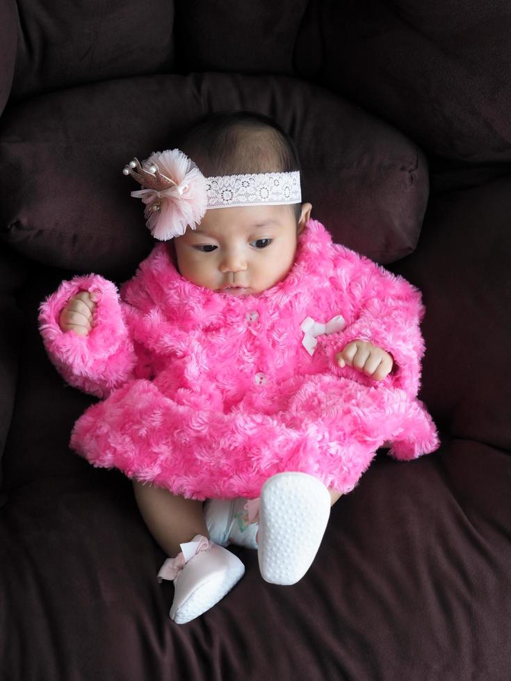 een Aziatische meisjesbaby die een roze overhemd draagt dat op de bank ligt met comfort foto