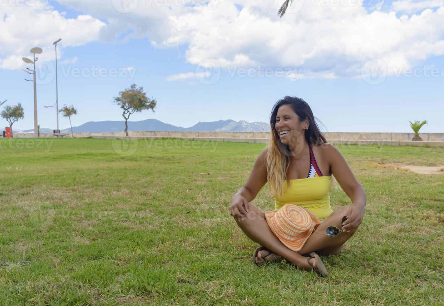 mooie latijnse vrouw 40 jaar oud, glimlachend zittend op het gras van een park in mallorca, balearen, vakantie concept foto