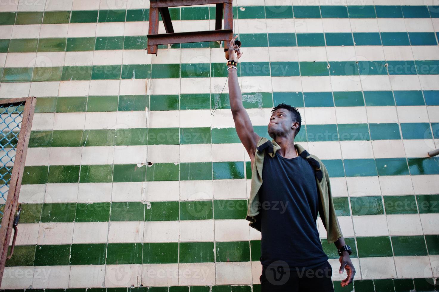 aantrekkelijke jonge Afro-Amerikaanse man in casual kleding die naast de betegelde muur staat. foto