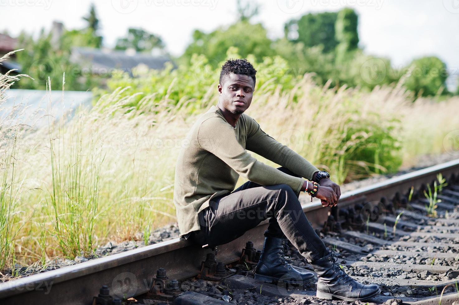 coole zwarte Afro-Amerikaanse man zit en poseert op de spoorlijn op het platteland. foto