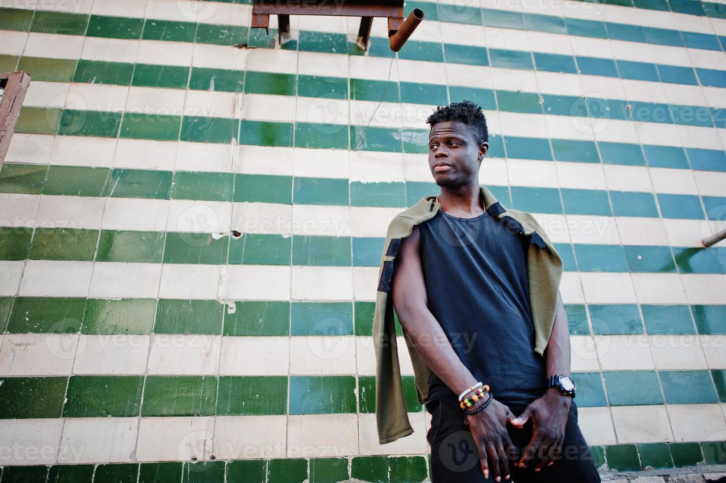 aantrekkelijke jonge Afro-Amerikaanse man in casual kleding die naast de betegelde muur staat. foto